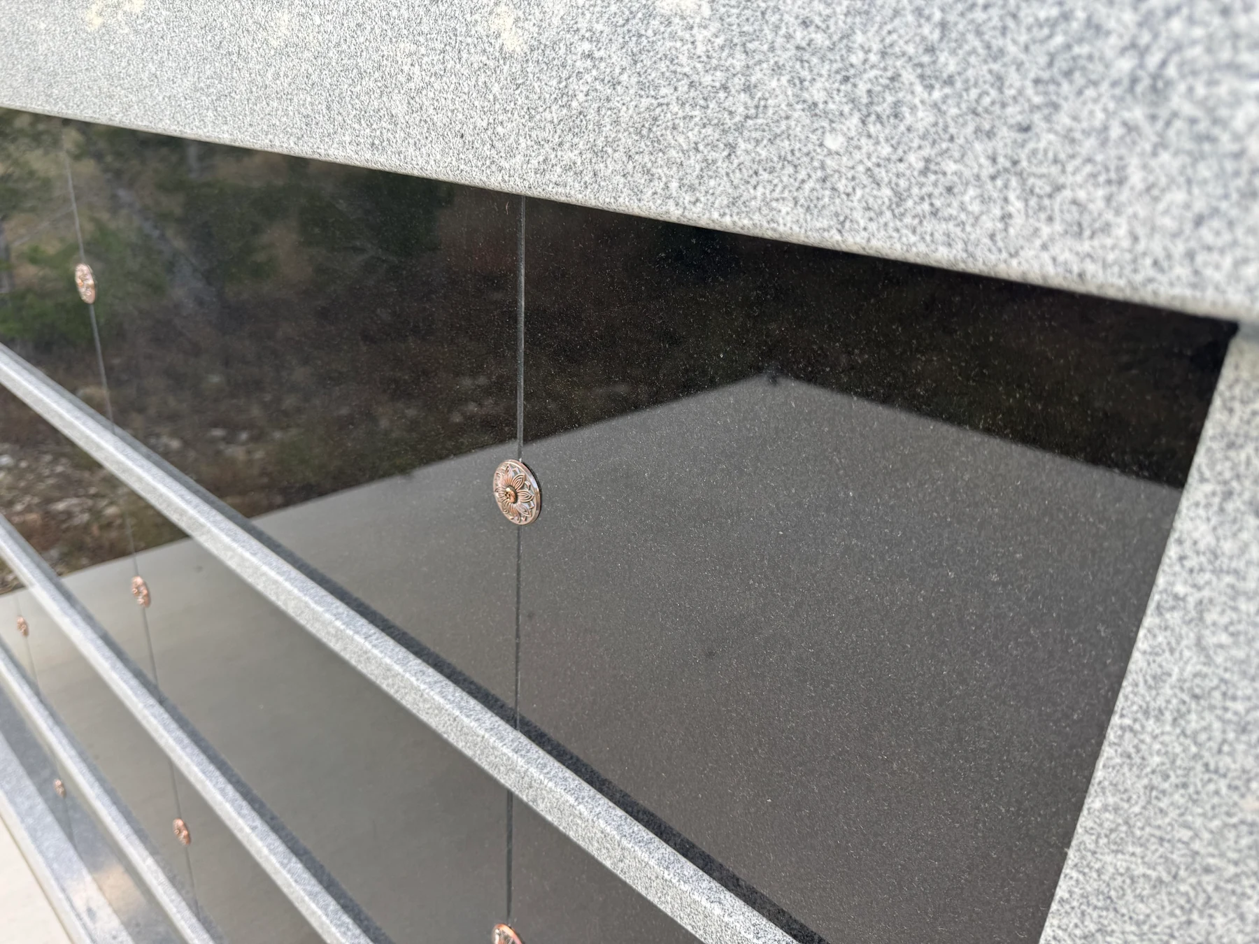 Close view of polished black granite, gray granite rails, and bronze rosette fasteners.