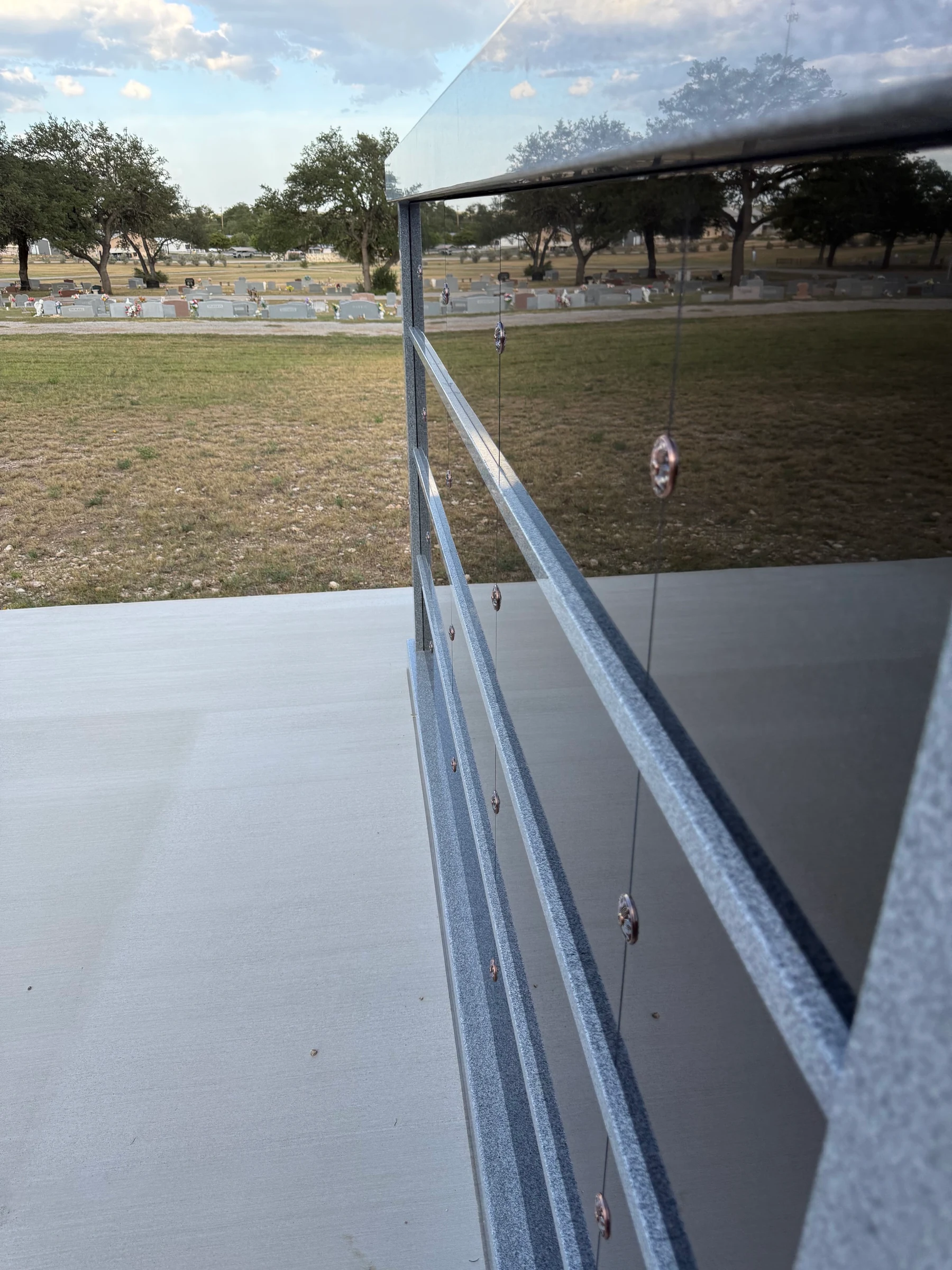 The columbarium’s polished face beside its concrete plaza, with open cemetery grounds beyond.