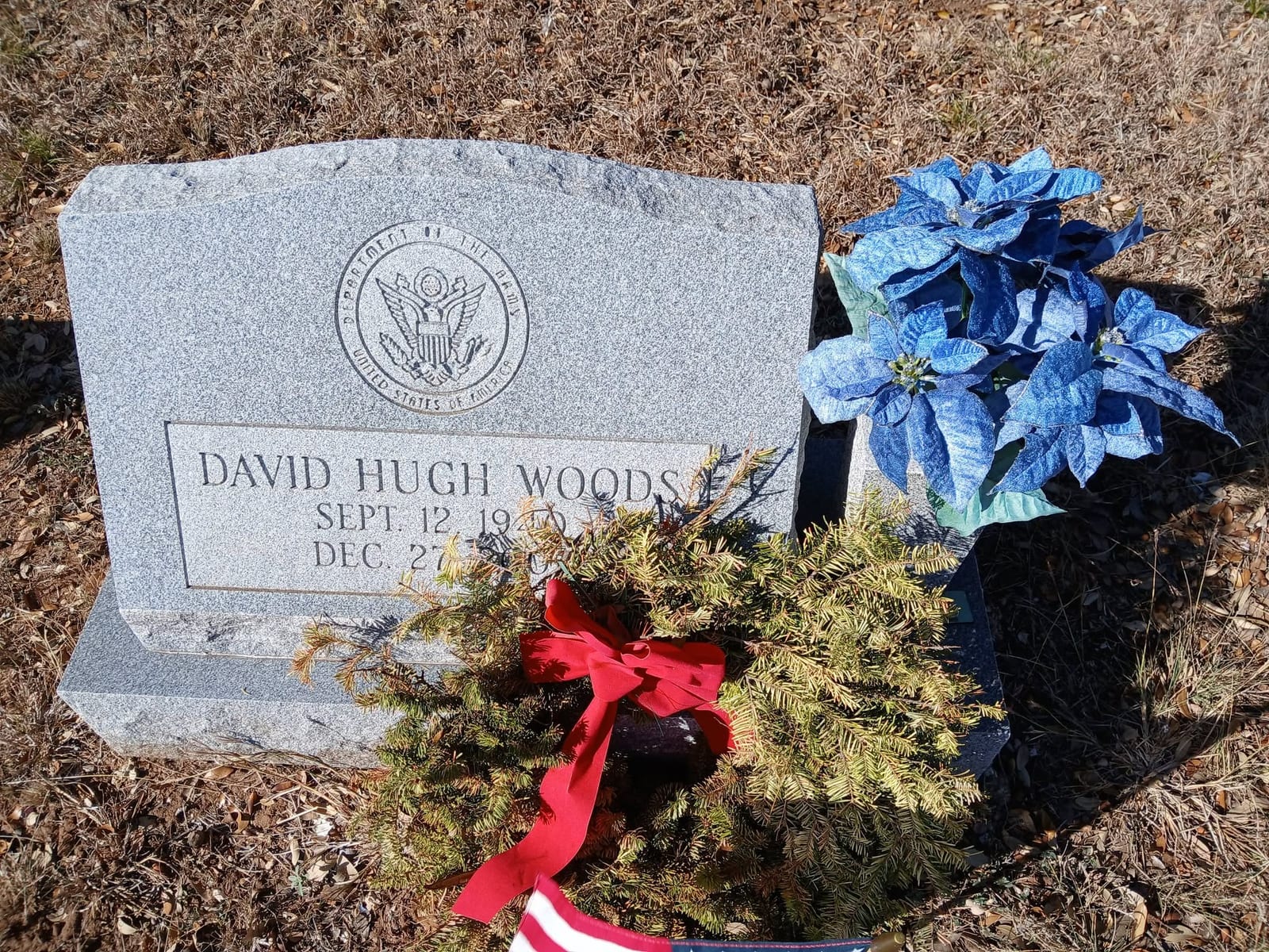 A Department of the Army headstone with a balsam wreath, a red bow, and a small American flag laid against it.